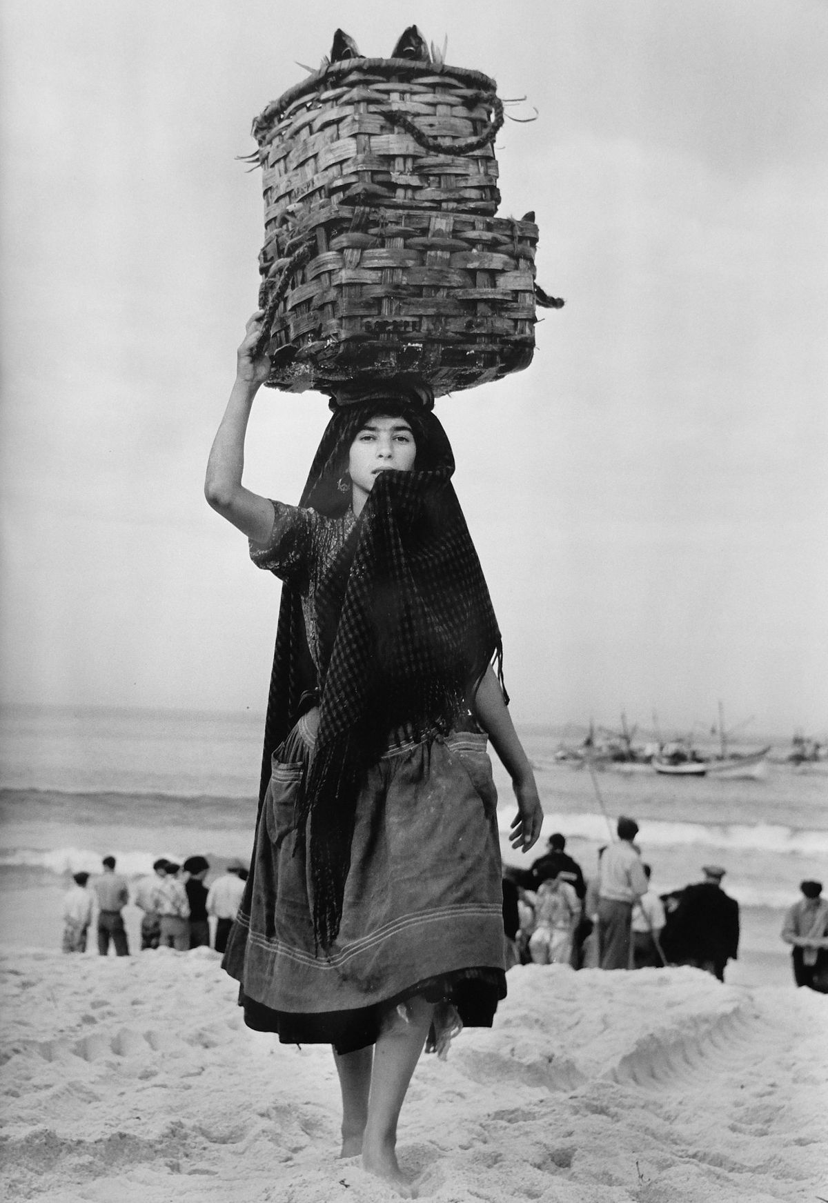Woman in traditional Portuguese dress carrying a basket of fish on her head on a Portuguese beach