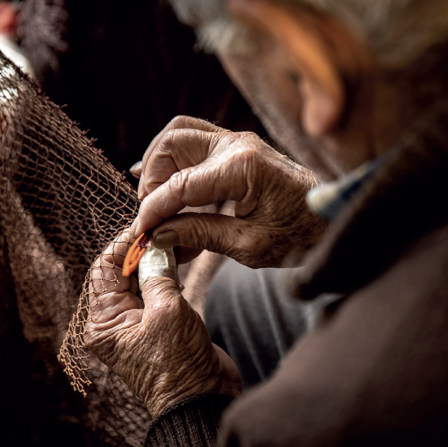 Hands repairing a fishing net, evoking coastal labor and tradition