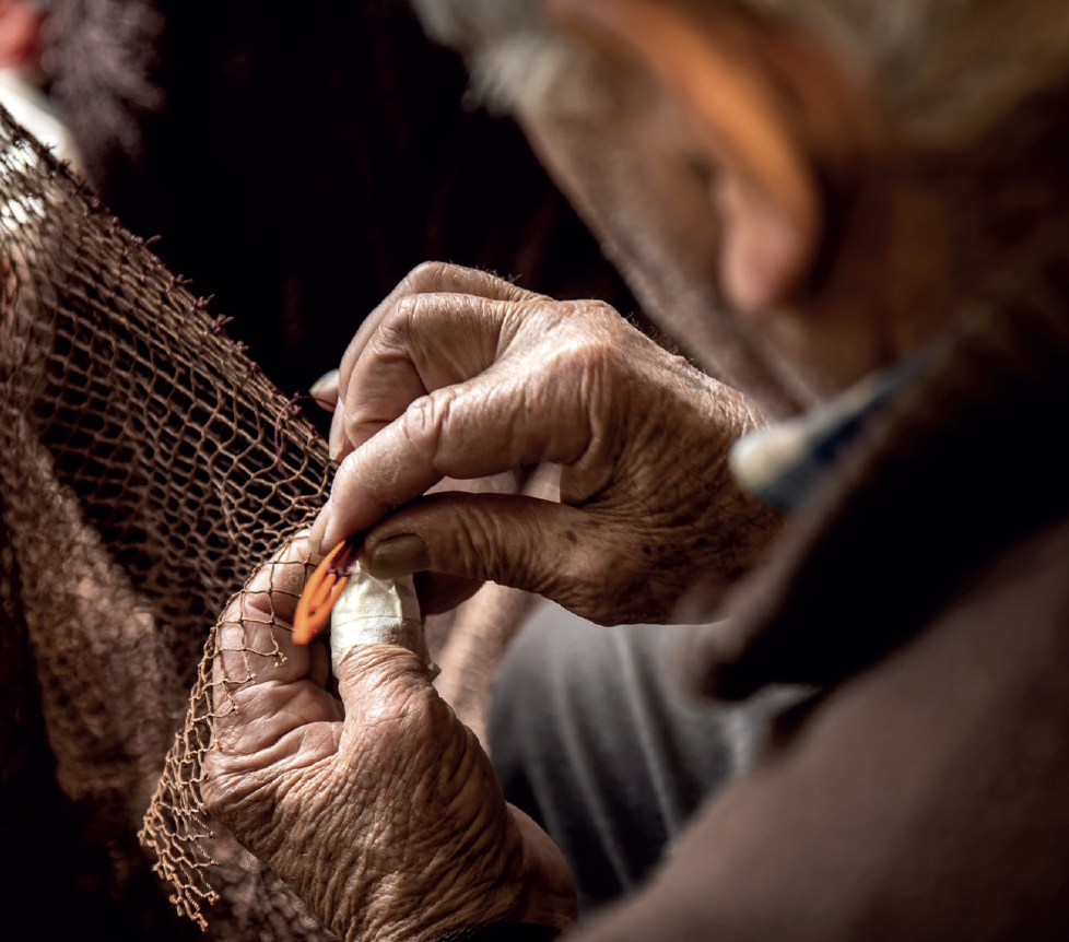A fisher carefully repairing a traditional fishing net by hand